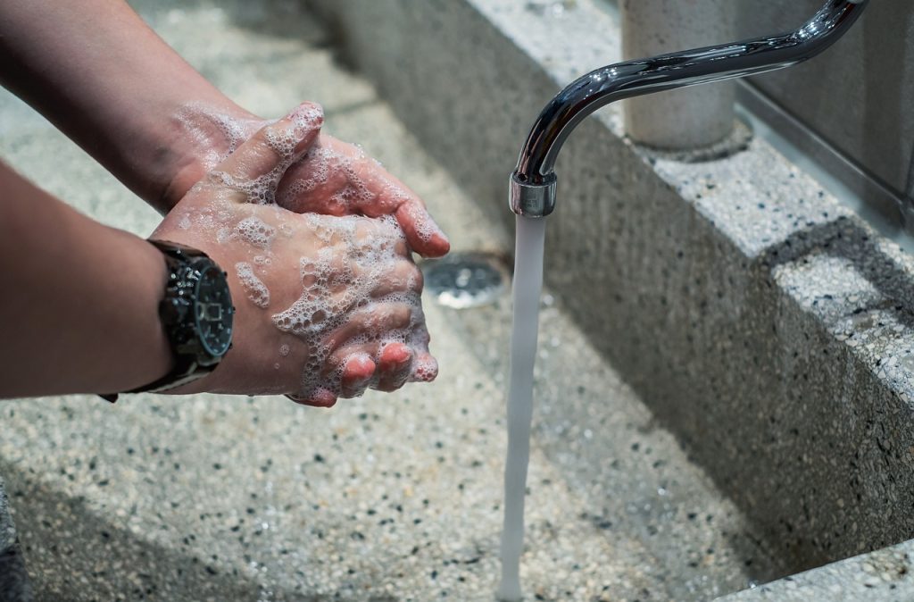 person rinsing air conditioner filter under faucet with soap