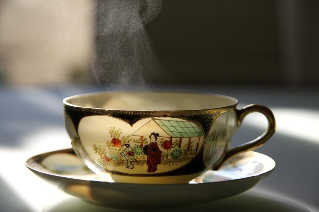 person warming hands around a hot cup of tea indoors