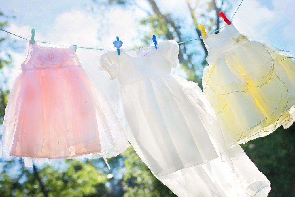 parent sorting and folding children's seasonal clothes on bed with storage bins nearby